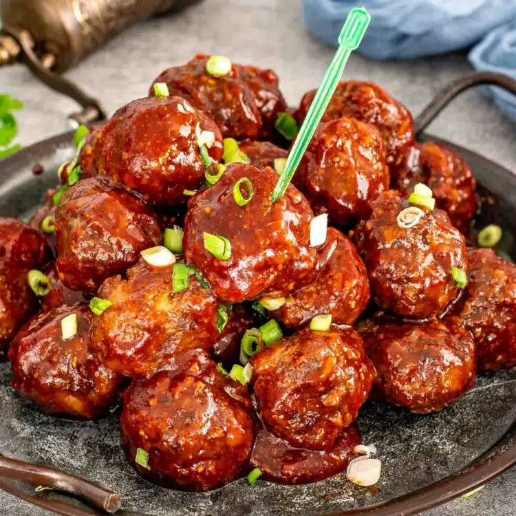 bbq meatballs in a metal plate garnished with green onions.