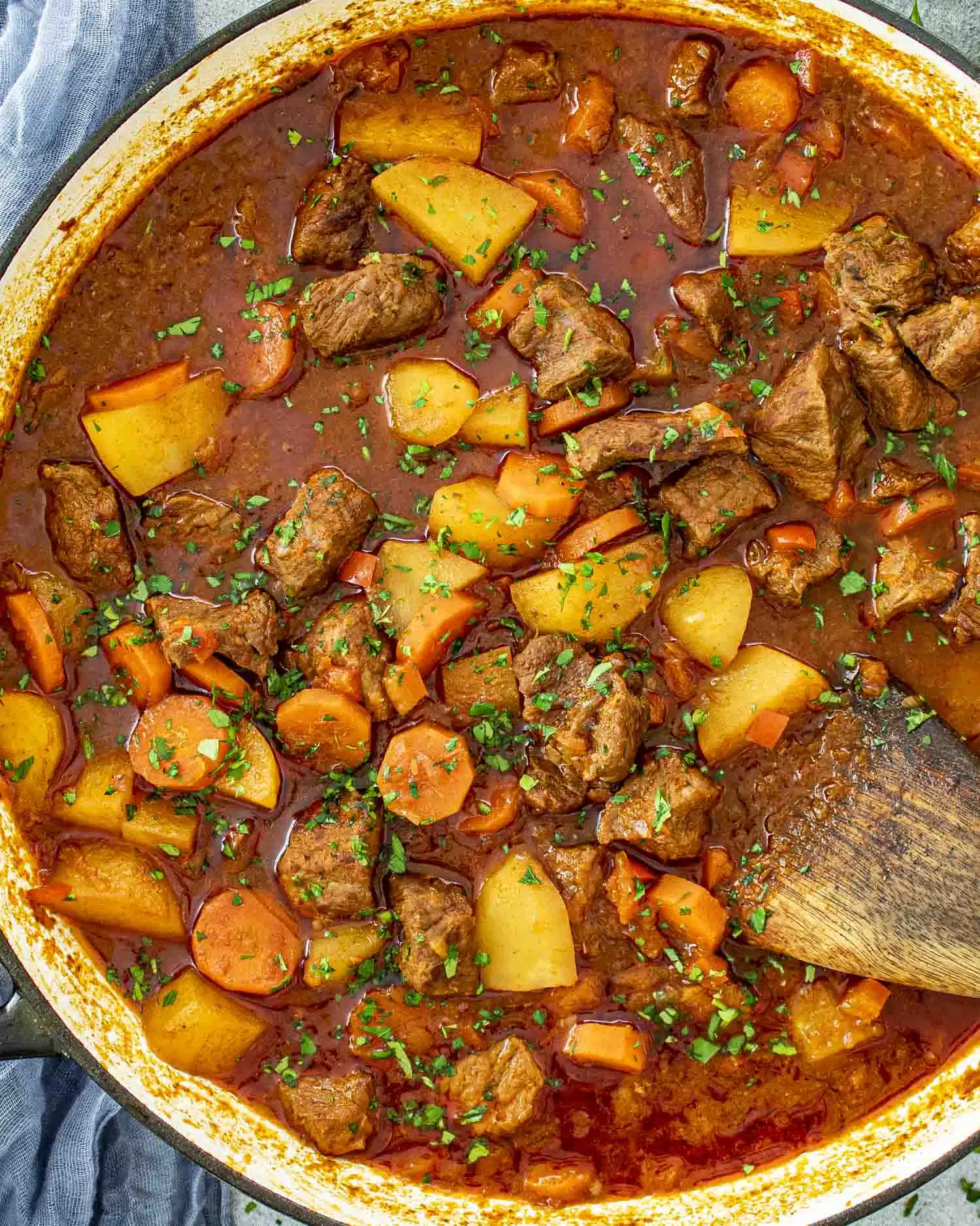 A close-up shot of a hearty Beef Goulash in a large Dutch oven. Tender chunks of beef, golden potatoes, and sliced carrots are simmered in a rich, deep-red paprika-infused broth. The dish is garnished with freshly chopped parsley, adding a pop of green.