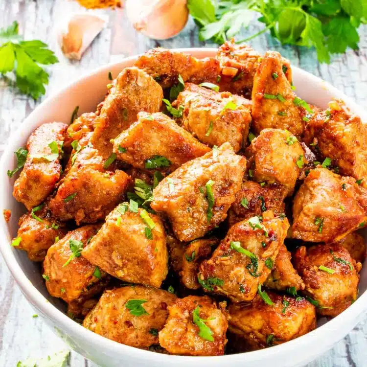 cajun pork bites garnished with parsley in a bowl.
