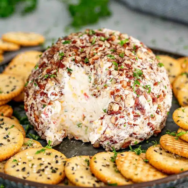 a cheese ball on a plate surrounded by crackers.