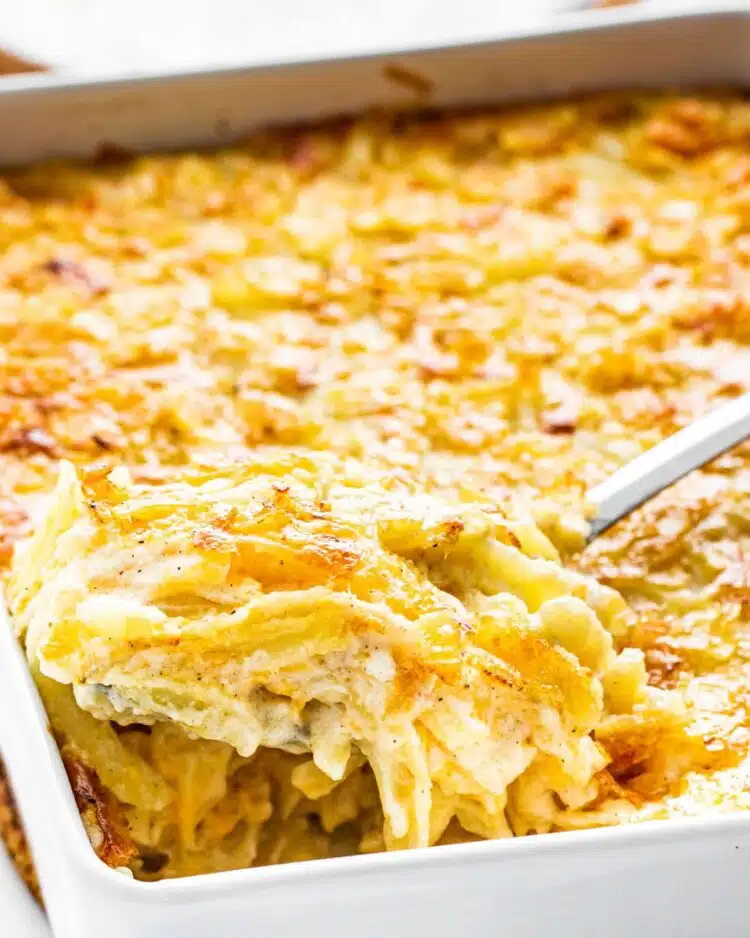 a serving spoon scooping out some cheesy potato casserole from a casserole dish