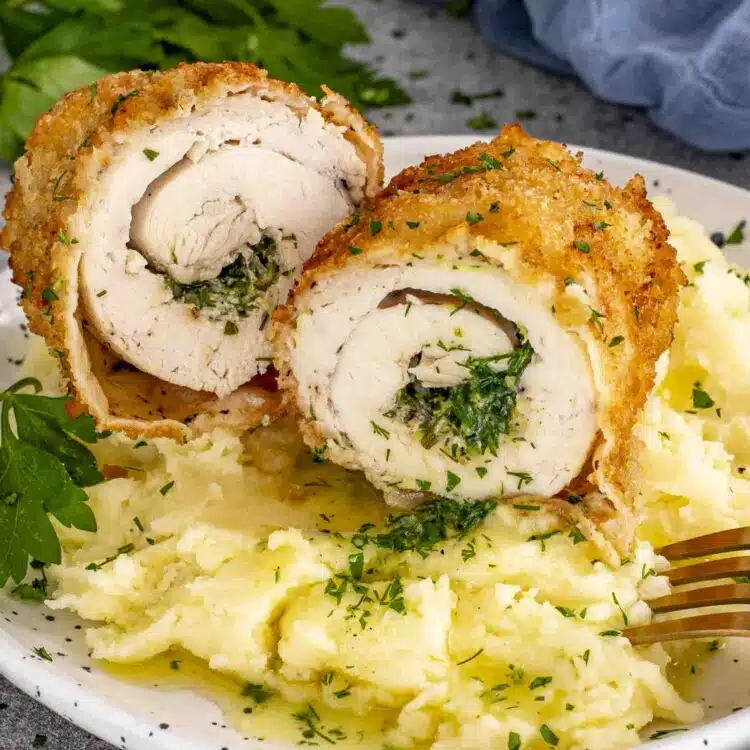 Sliced Chicken Kiev showing garlic herb butter center, served over creamy mashed potatoes, sprinkled with parsley.
