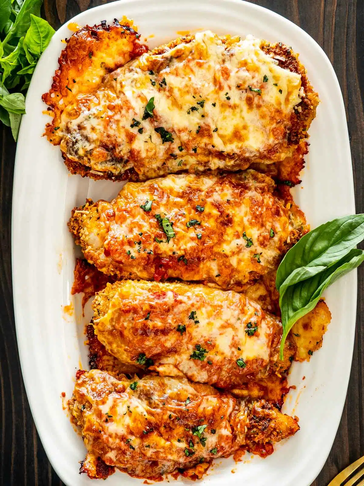 4 pieces of chicken parmesan on a white platter.