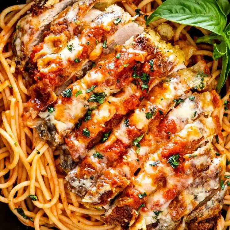 sliced up chicken parmesan on a bed of spaghetti in a black bowl.