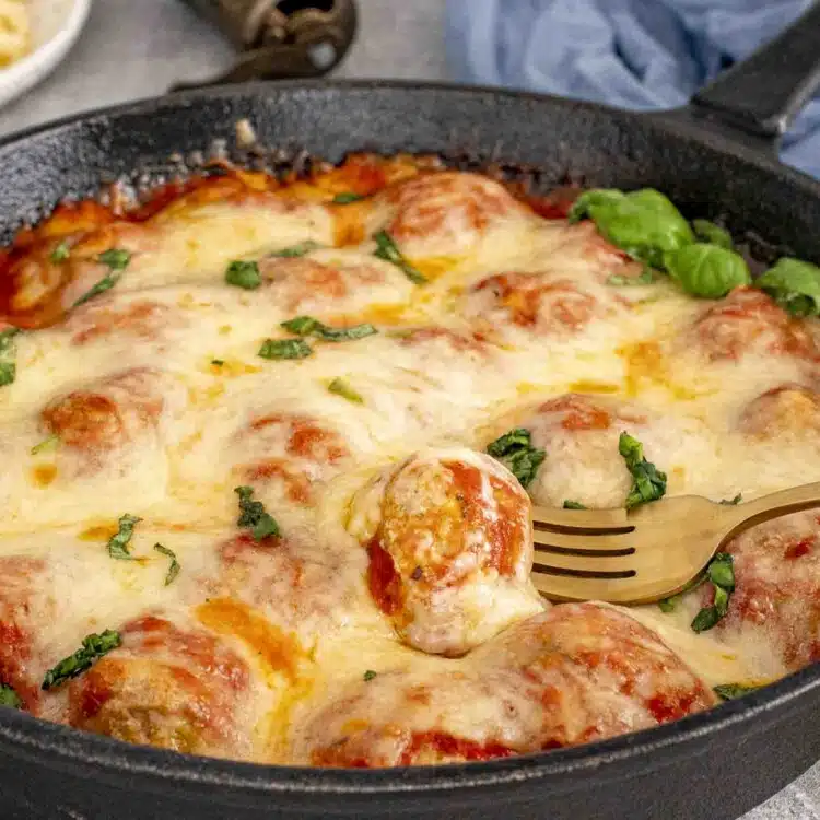 fresh out of the oven chicken parmesan meatballs in a cast iron skillet garnished with some fresh basil.