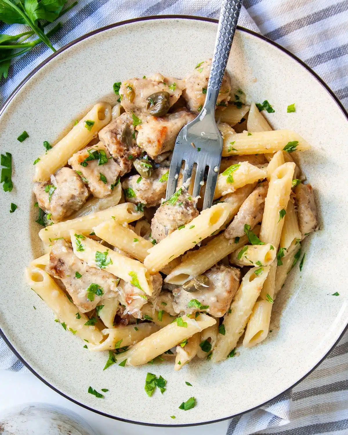 Chicken Piccata Pasta with a fork in it on a beige plate