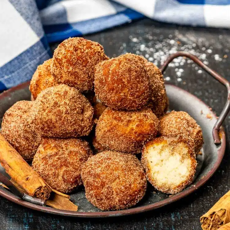 a metal plate with stacked cinnamon sugar donuts holes.