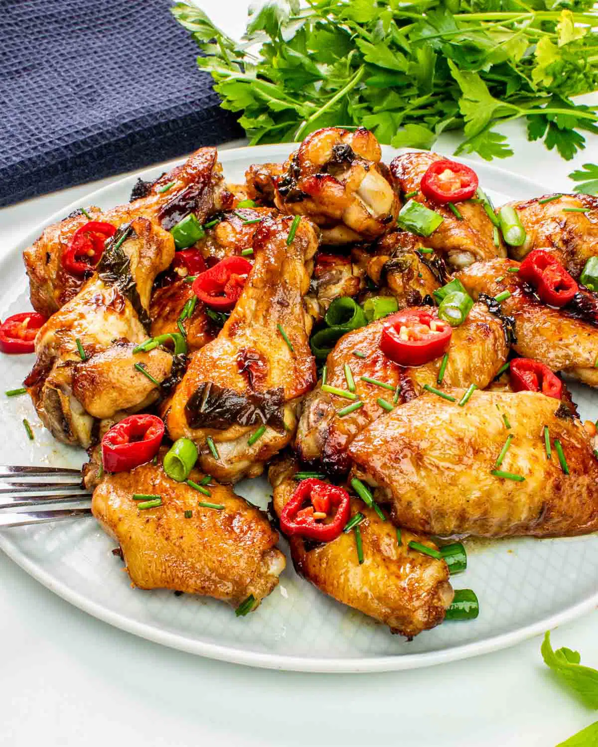 coca cola wings on a white plate garnished with red chili peppers.