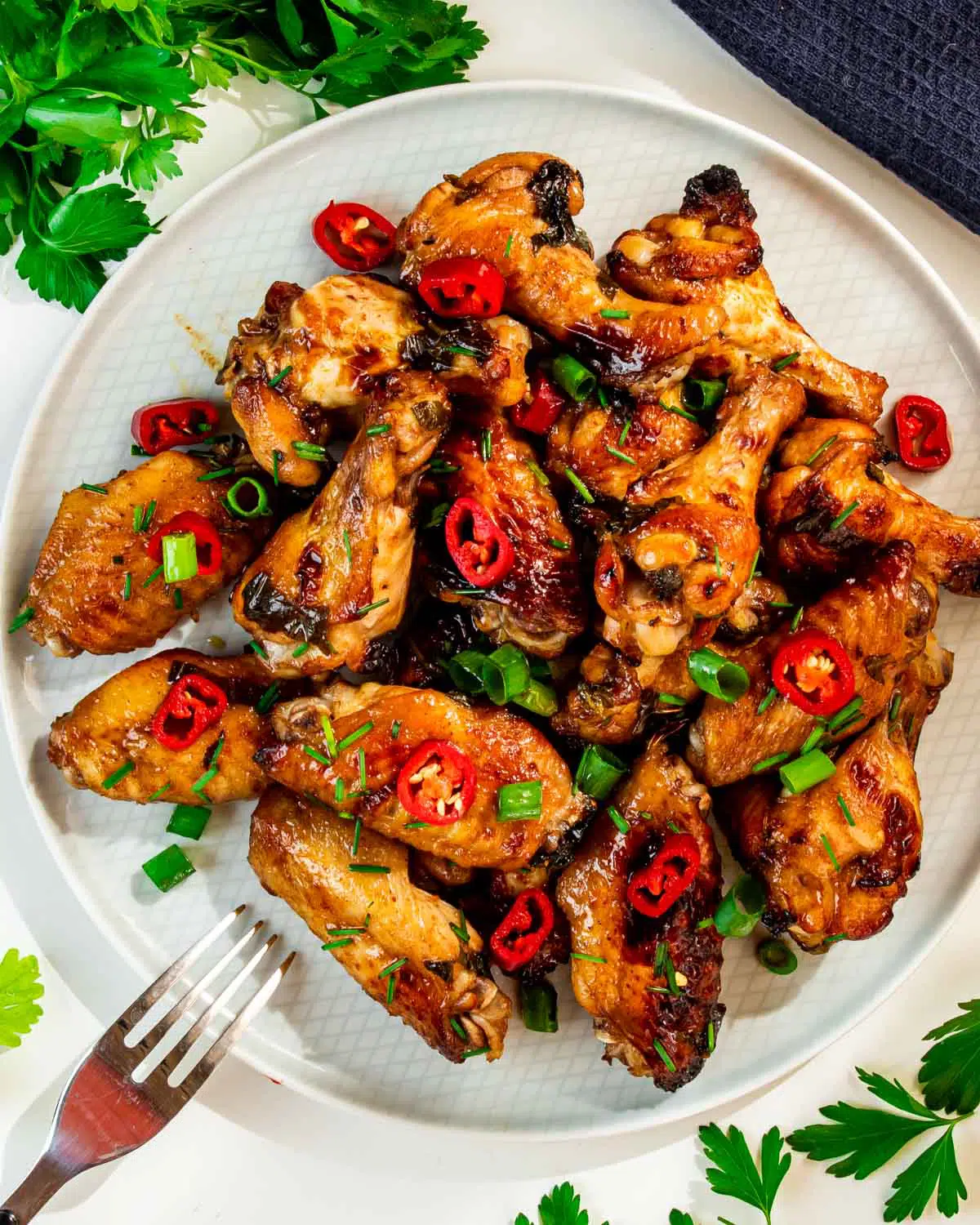 coca cola wings on a white plate garnished with red chili peppers.