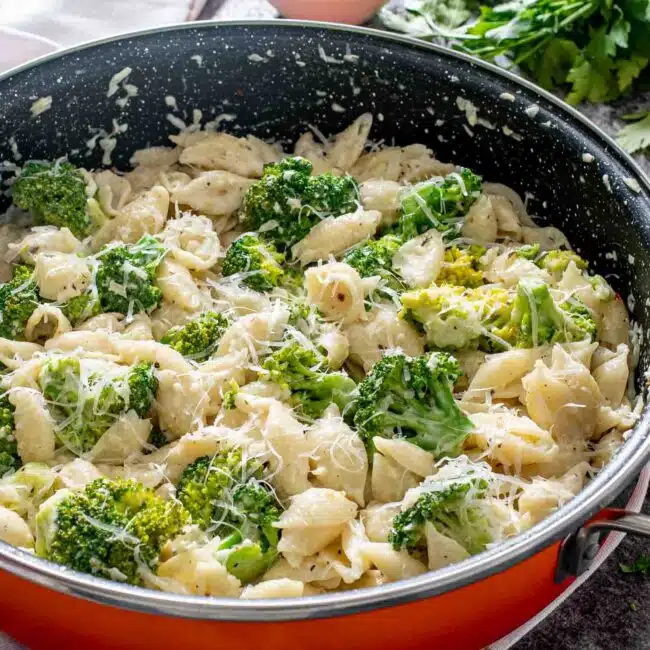creamy broccoli pasta in a skillet with a wooden spoon inside.