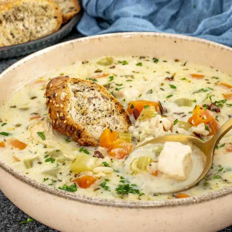 A warm, comforting bowl of creamy chicken wild rice soup, filled with tender chunks of chicken, diced carrots, celery, and wild rice in a rich, herb-infused broth.