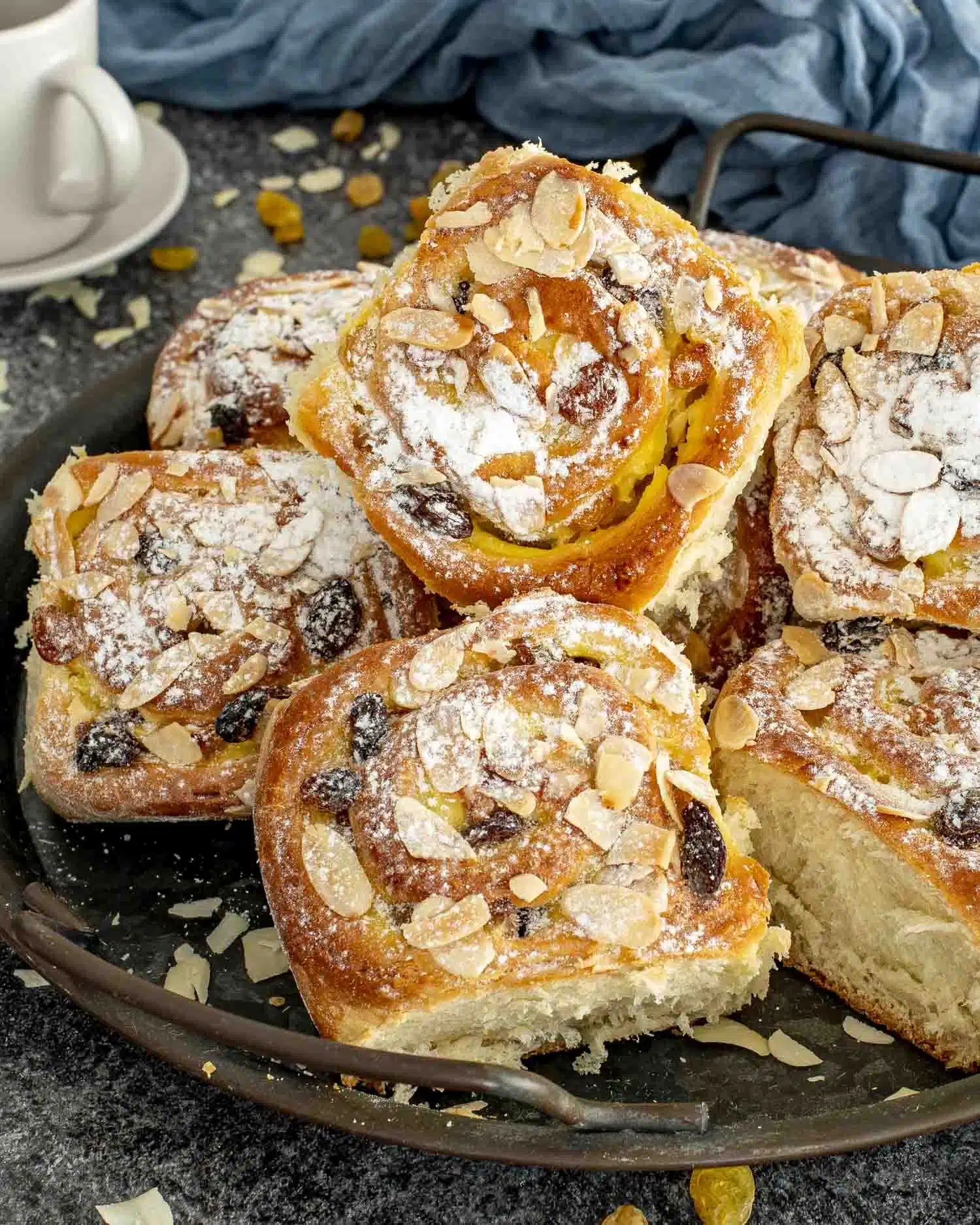 a few custard raisin rolls on a dark plate, dusted with icing sugar.