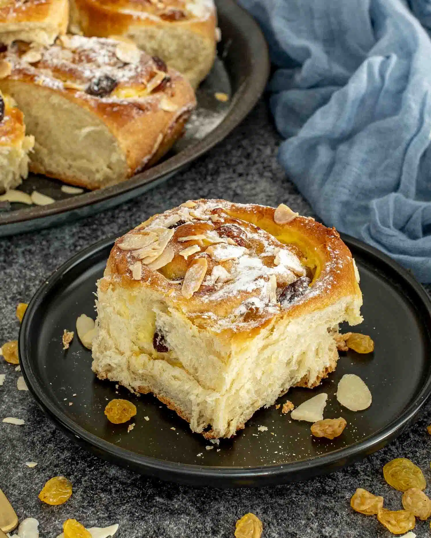 a custard raisin roll on a black plate dusted with icing sugar.