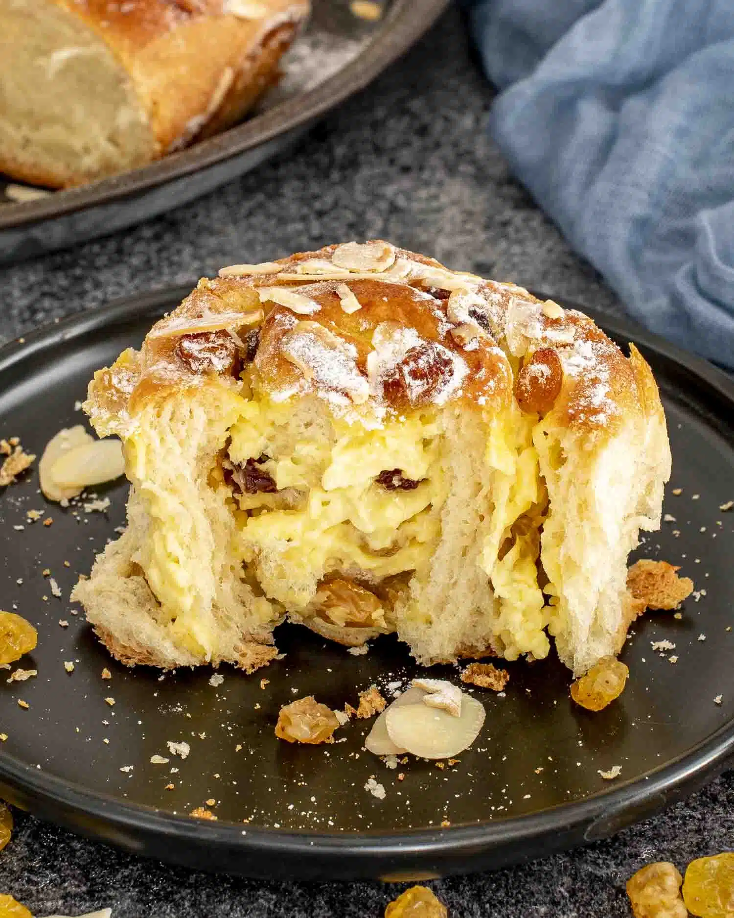 a custard raisin roll on a black plate, half eaten, dusted with icing sugar.