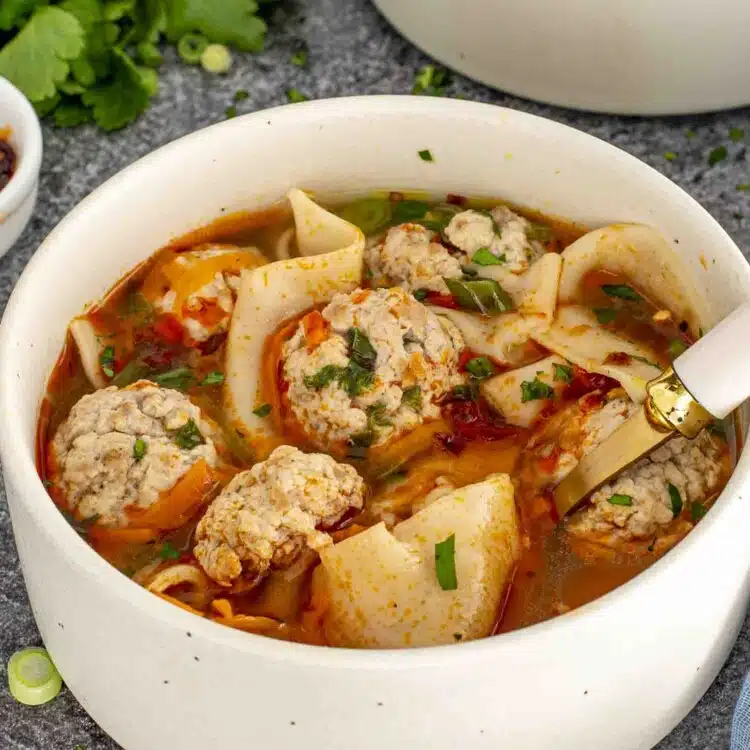 a beige bowl loaded with deconstructed wonton soup and garnished with chili oil.