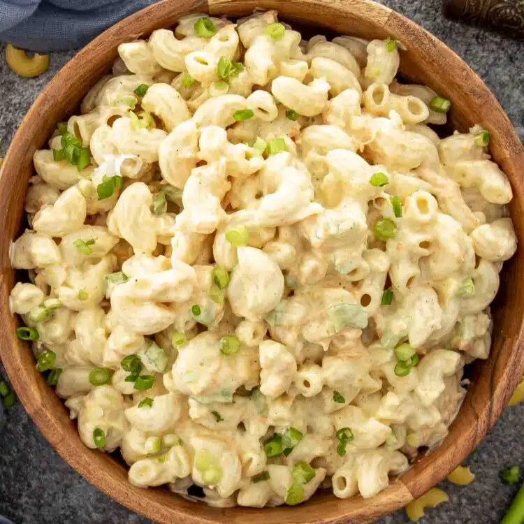 Creamy Hawaiian macaroni salad in a wooden bowl garnished with sliced green onions, set on a gray textured surface.