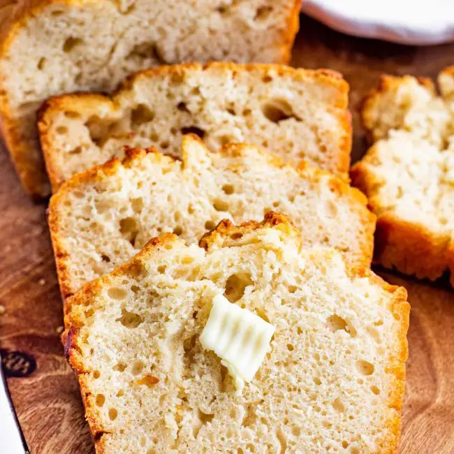 3 slices of honey beer bread on a cutting board with a pat of butter.