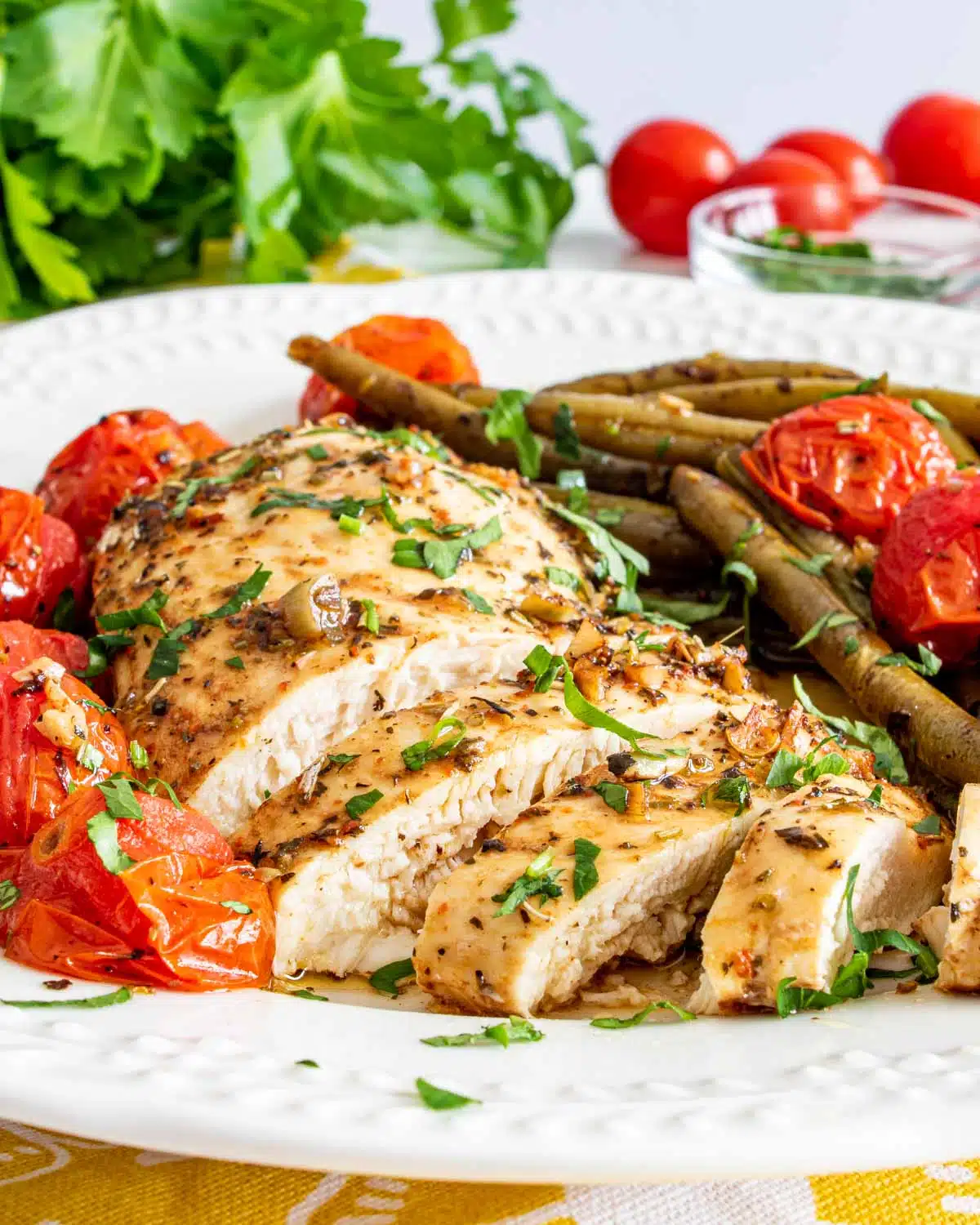 italian chicken breast sliced up with roasted green beans and tomatoes on a white plate.