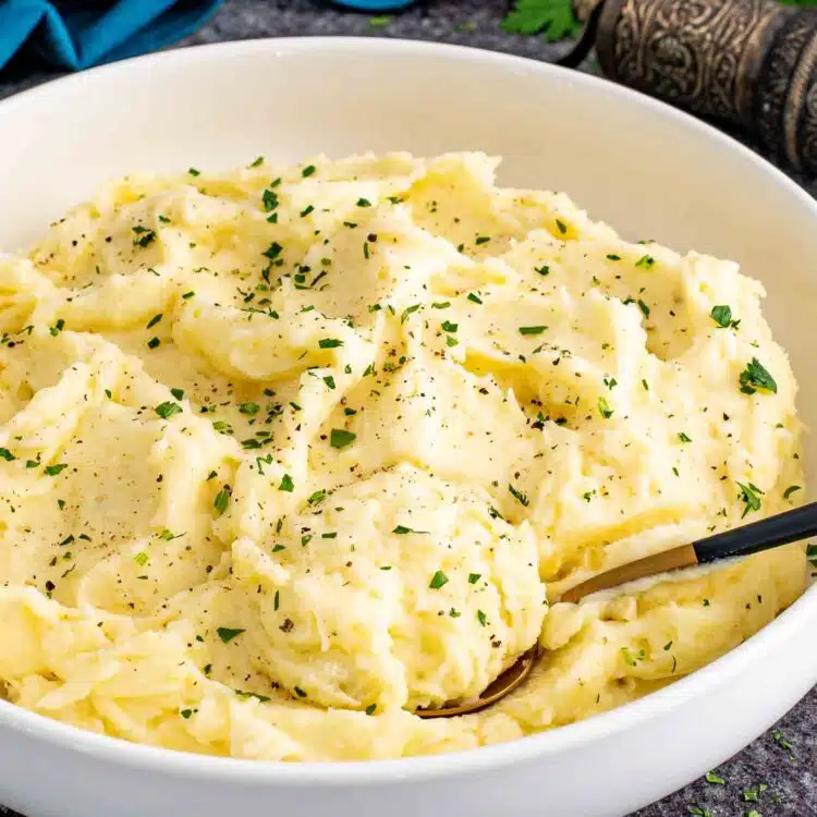a big white bowl with freshly made mashed potatoes and garnished with a bit of parsley.