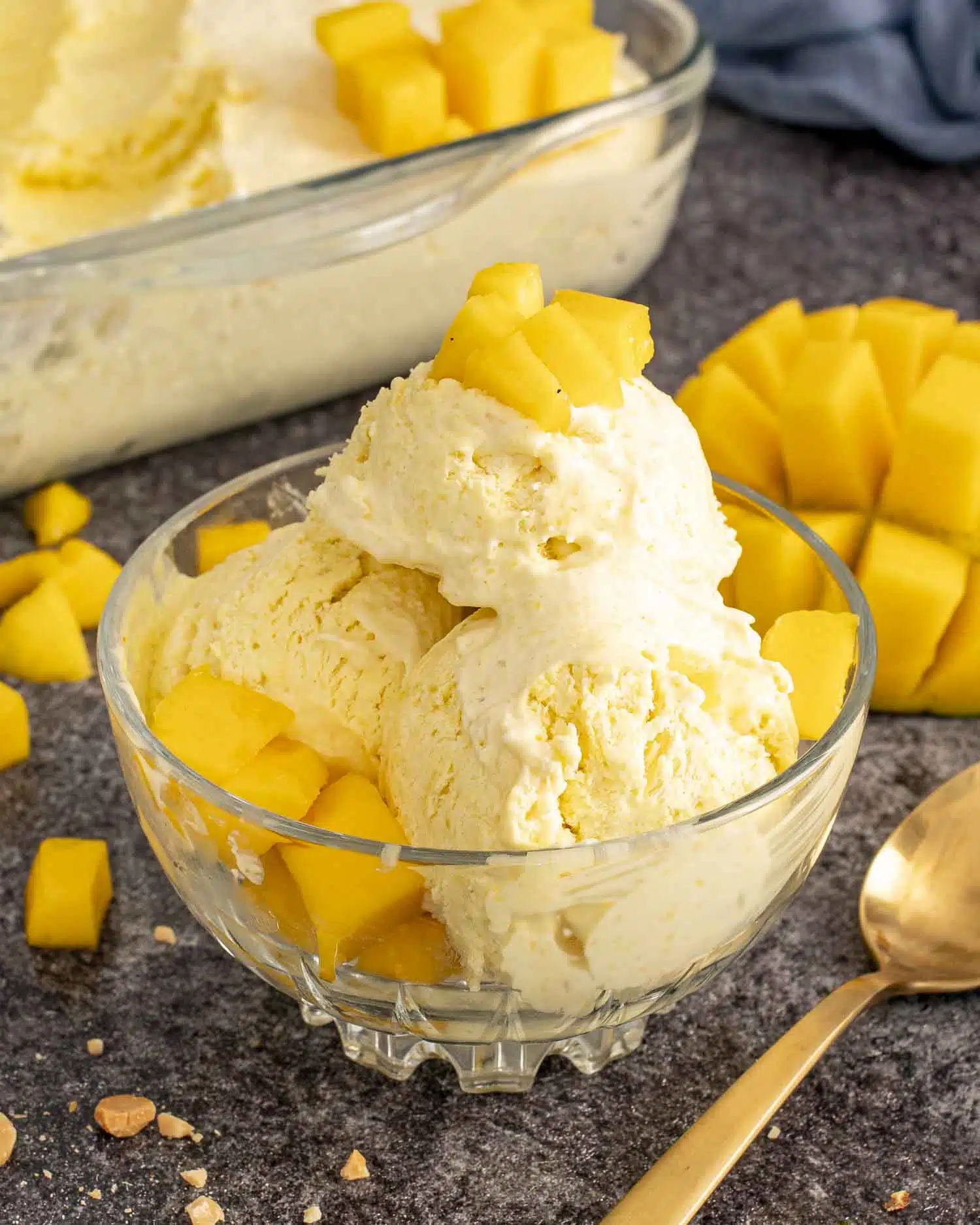 Mango ice cream served in a bowl with diced mango on top, set on a dark textured surface.