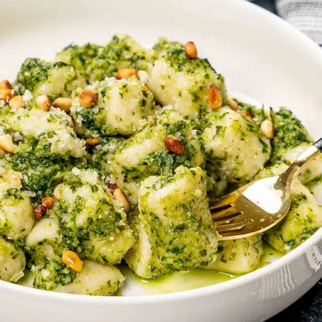 a serving of pesto gnocchi with toasted pine nuts in a white bowl.