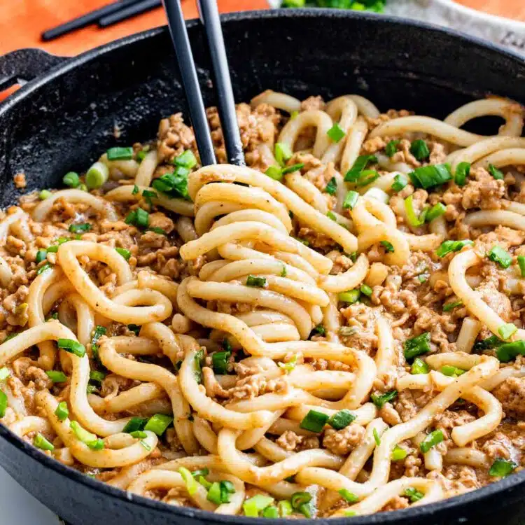 overhead of quick chicken peanut noodles in a skillet with chopsticks twirling some noodles.