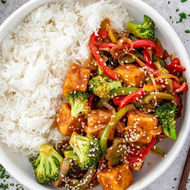 a serving of spicy tofu stir fry next to a serving of rice in a white plate.