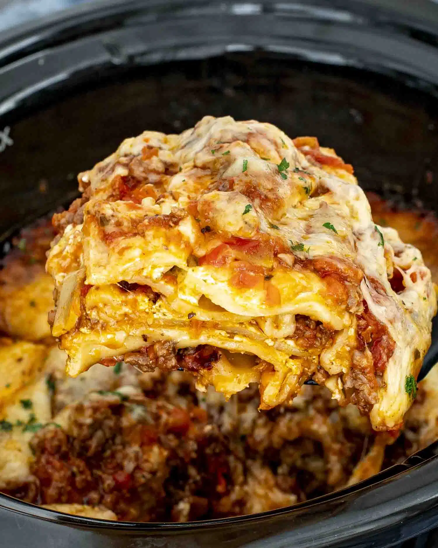 a spatula lifting a slice of lasagna from the slow cooker.