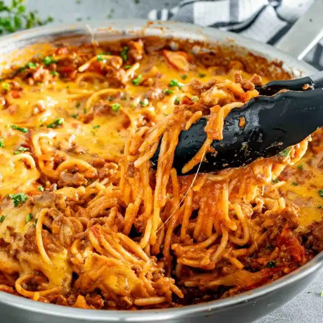 freshly made taco spaghetti in a stainless steel skillet topped with cheese and garnished with parsley.