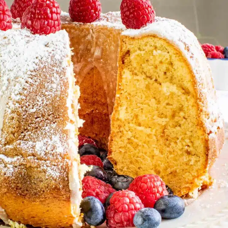 a gorgeous vanilla bundt cake sprinkled with powdered sugar and topped with berries with a slice cut out of it.